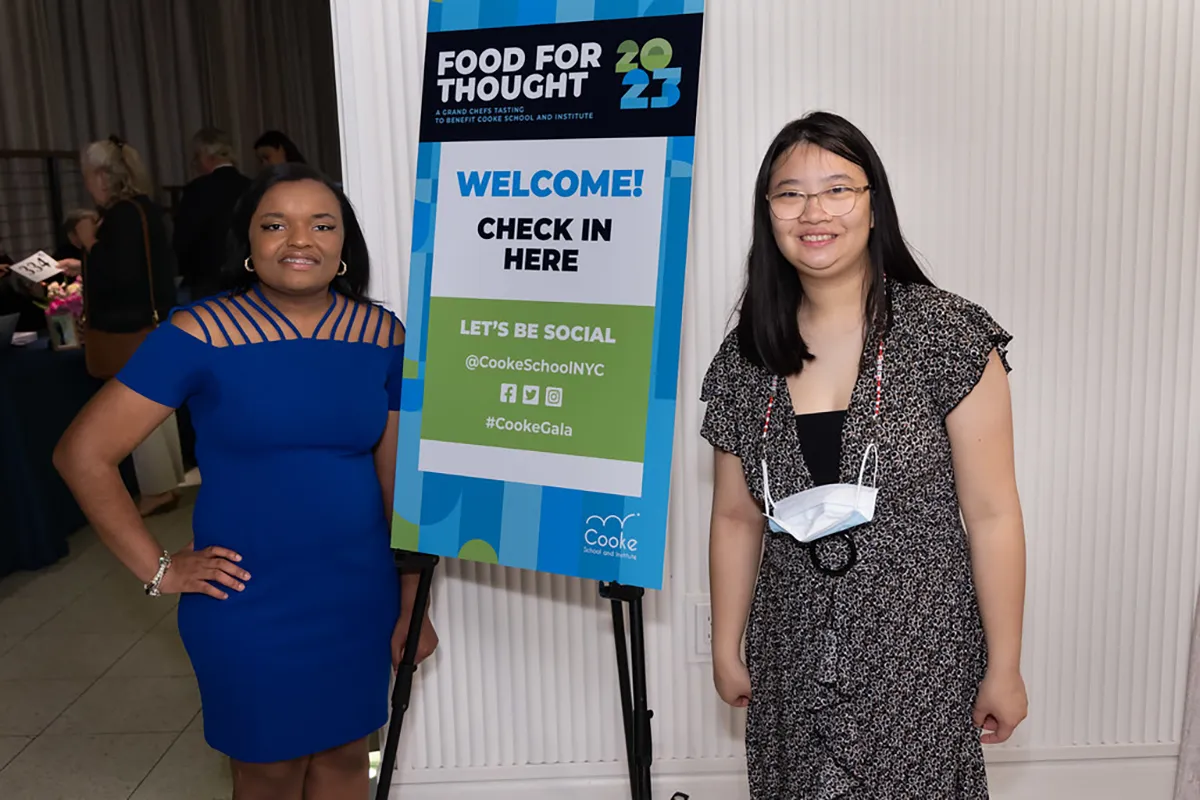 Two Cooke School Food for Thought Gala Attendees standing alongside a check in banner.