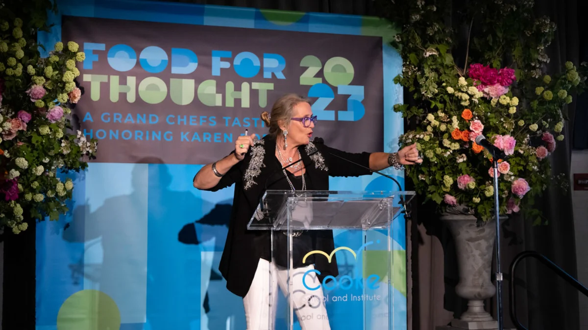 A speaker at the Food for Thought Gala standing in front of a branded backdrop.