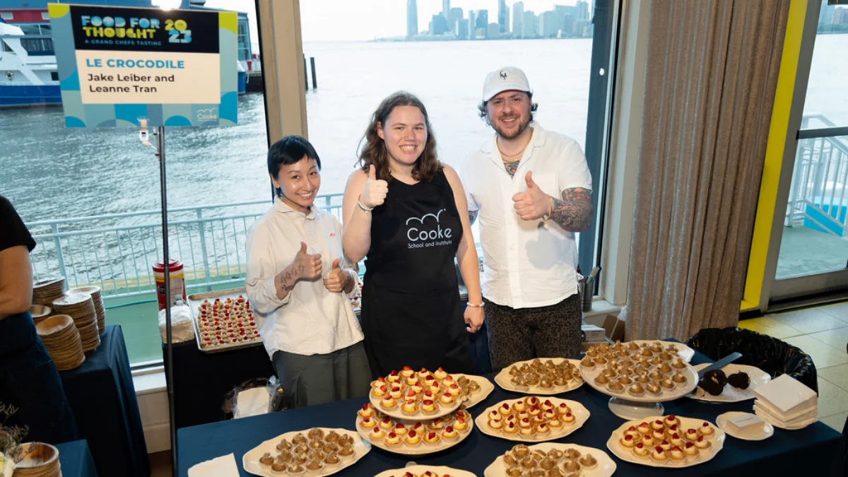 Chefs and a student at the event standing behind a table with a branded Food for Thought sign.