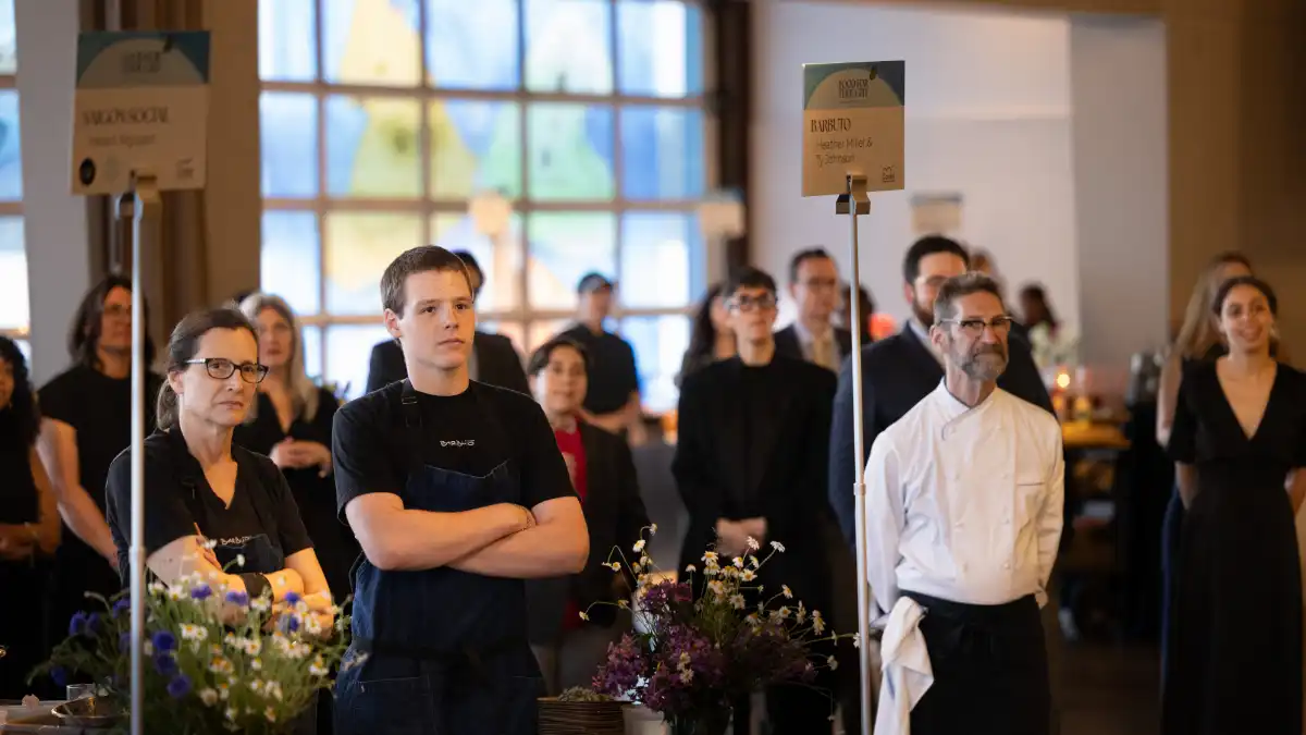 Chefs and a student at the event standing behind a table with a branded Food for Thought sign.