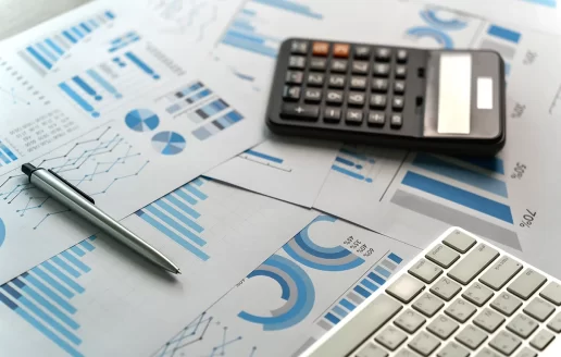 A photo of printed marketing charts and graphs, with a pen, calculator, and a keyboard on top of them.