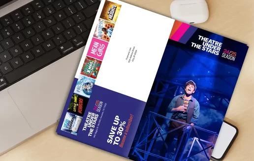 The acquisition brochure for Theatre Under the Stars open to the front and back cover on a desk.