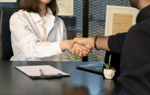 Two professionals shaking hands across a desk to begin a partnership